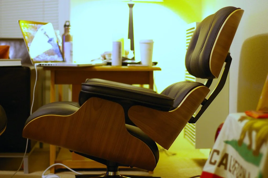Side view of the Eames Lounge Chair and ottoman, showing layered wood shells and dark leather cushions.