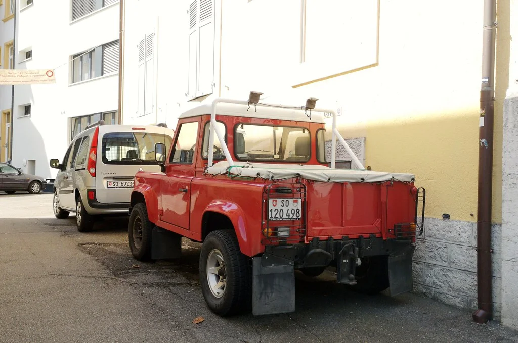 Land Rover Defender: An upright utility vehicle with a squared body, exposed hardware, high stance, and simple openings.