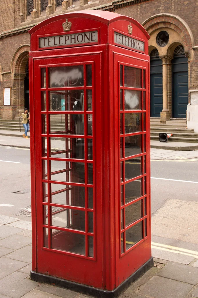 London Red Telephone Box: A freestanding red kiosk with repeated glass panes, a domed top, and crown lettering.