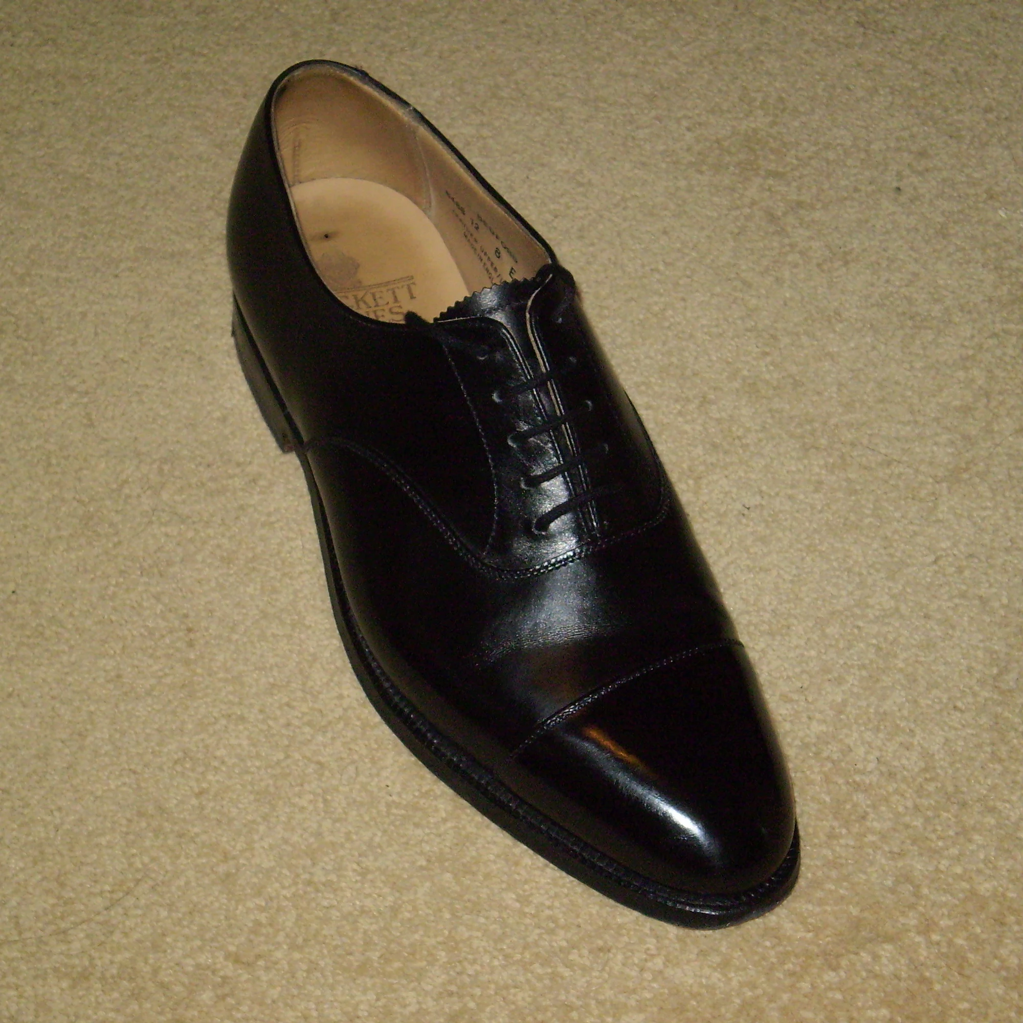 Oxford Shoe: A single black Oxford shoe photographed close up, with closed lacing, a cap toe, and layered leather panels.
